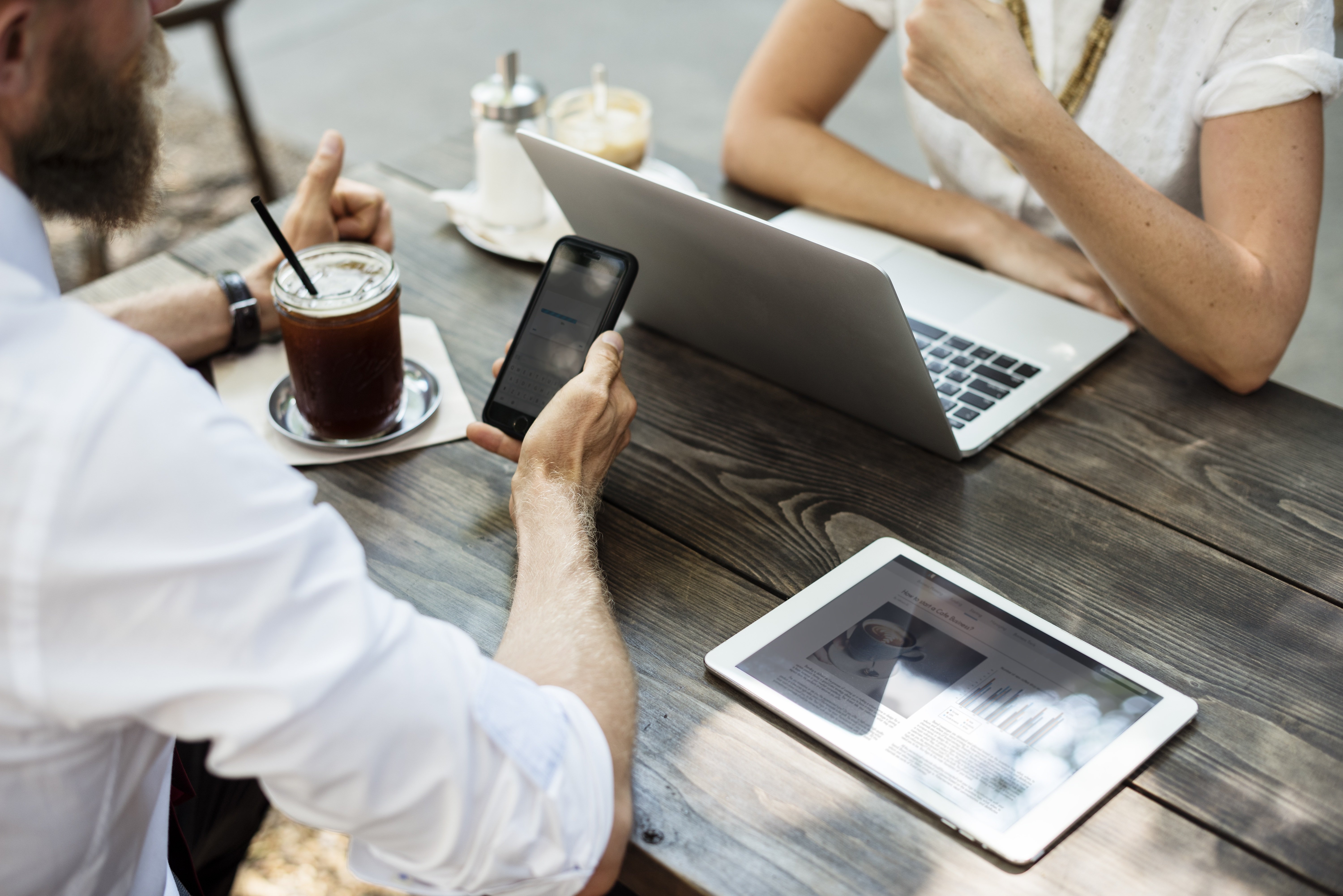Zwei Personen sitzen gegenüber an einem Tisch. Zwischen ihnen steht ein geöffneter Laptop und ein Tablet liegt daneben.