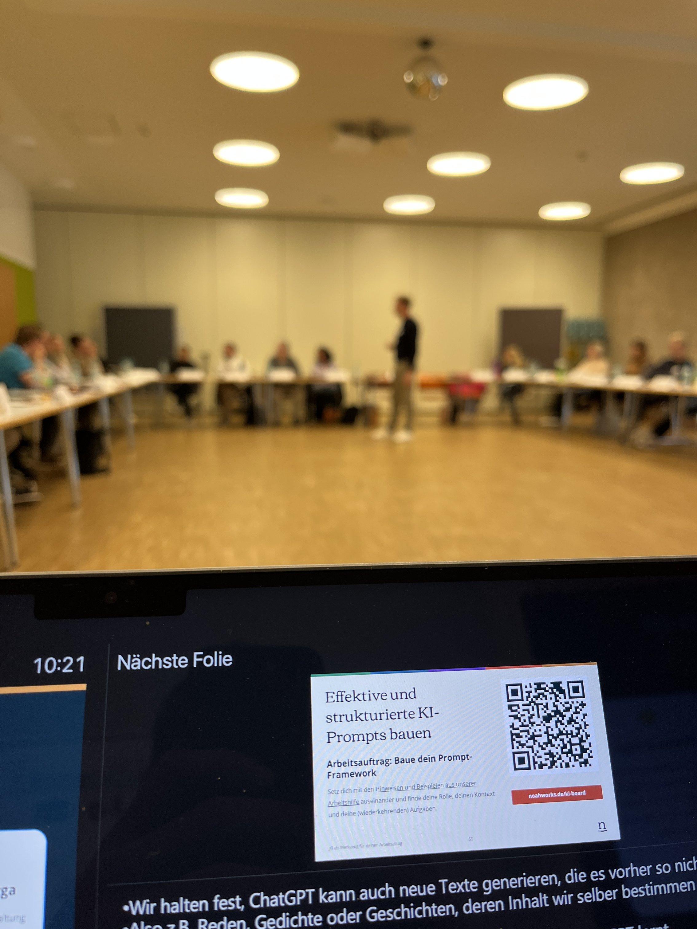 Blick auf den Laptop-Monitor mit Folien darauf - im Hintergrund steht der Referent Christian verschwommen für den Teilnehmenden
